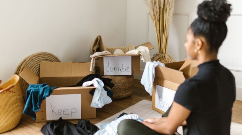 Kobieta segreguje odzież do kartonowych pudeł z napisami "Keep", "donate" i "trash".